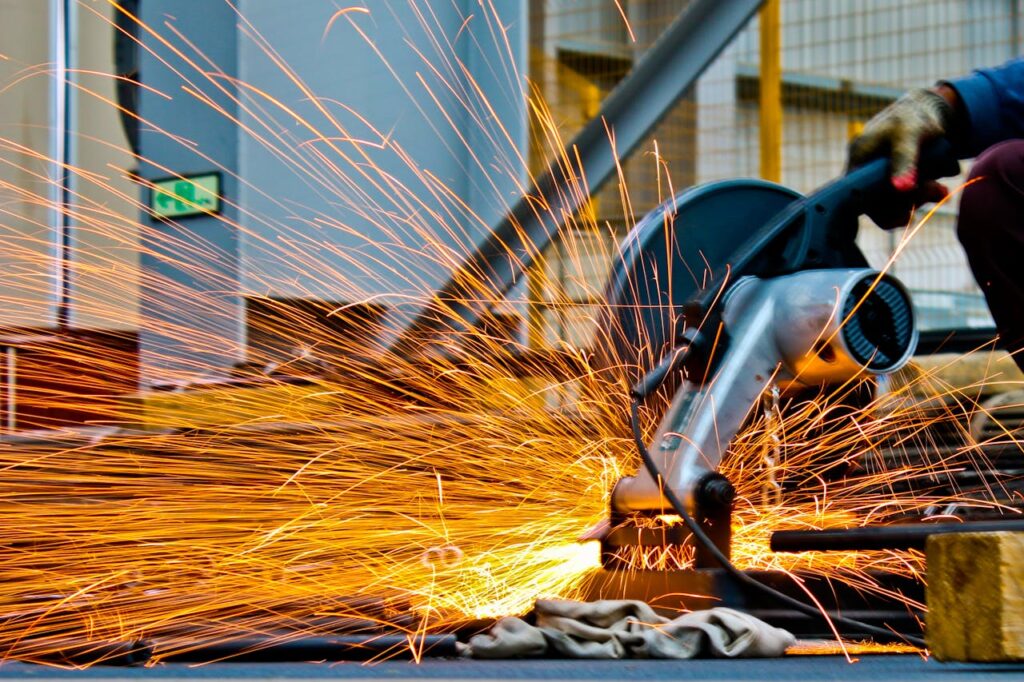 pexels-photo-1145434 A worker operates a grinder cutting metal, creating a vibrant display of sparks in an industrial setting.